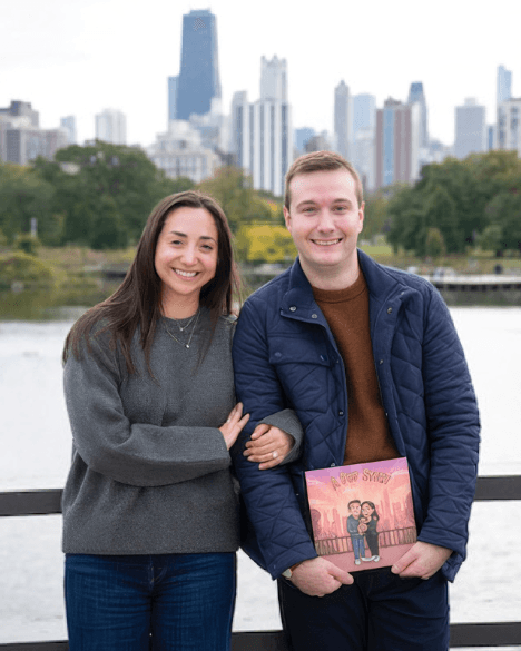 Un couple souriant au bord du lac, devant les gratte-ciel de la ville, tenant leur livre de mariage personnalisé avec leur portrait illustré en couverture